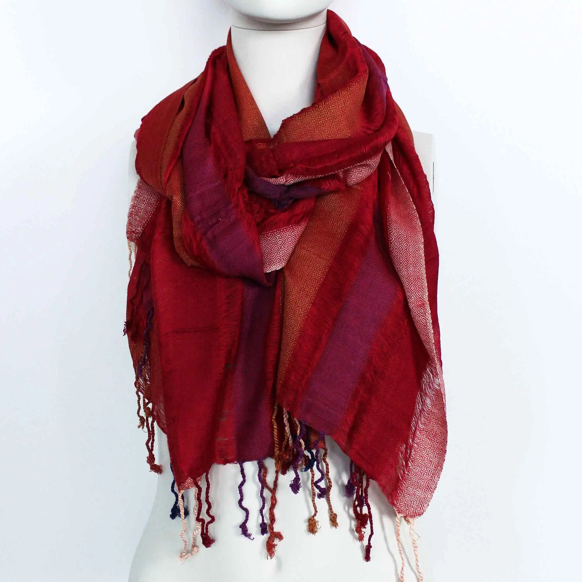 Bufanda bohemia grande en tonos rojos y púrpuras, con patrón geométrico, textura tejida y flecos en los extremos.