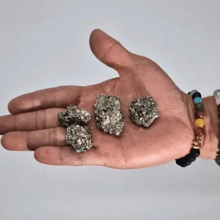 Piedras de pirita brillante, color gris metálico, en la mano, ideal para joyería y decoraciones.