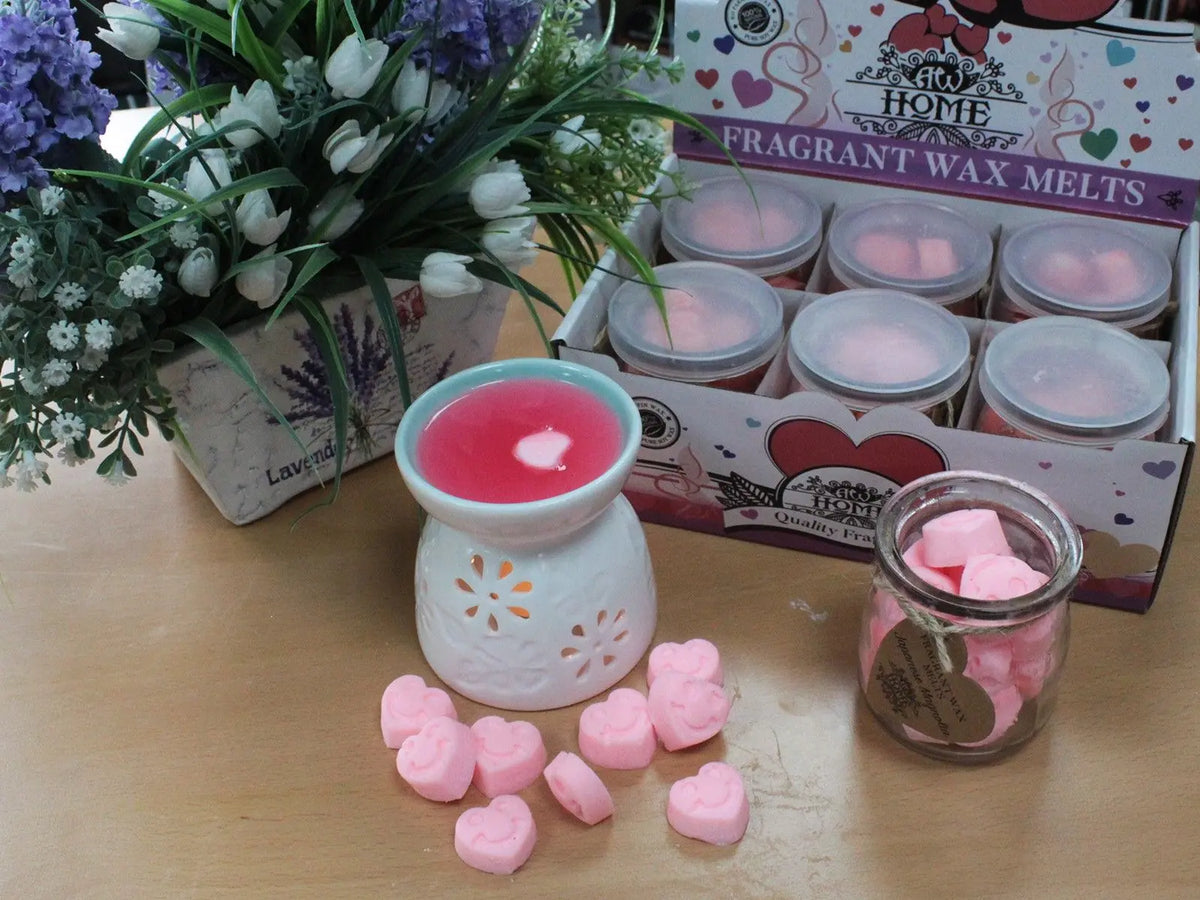 Difusor de cerámica con cera rosa fundida, junto a tarros con corazones de cera aromática y flores decorativas.
