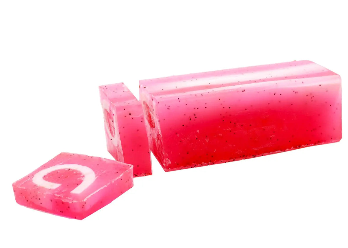 Jabón artesanal traslúcido rosa con puntos negros, forma rectangular y cortes, sobre fondo blanco.
