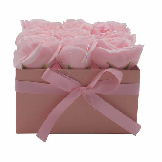 Caja cuadrada rosa con nueve rosas de jabón del mismo color, decorada con un lazo de cinta satinada a juego.