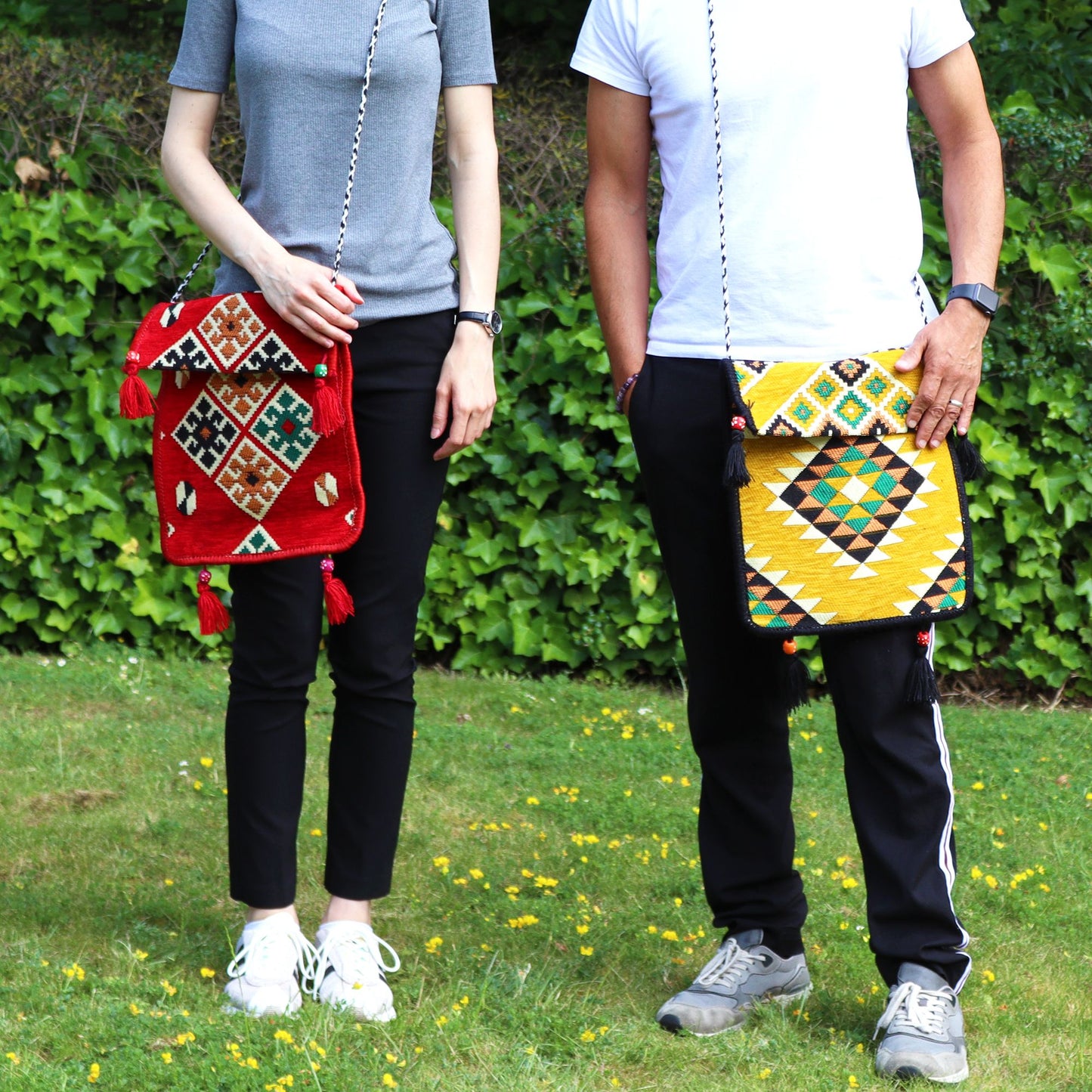 Dos personas portan bolsos bandolera de estilo Kilim con patrones geométricos coloridos y borlas decorativas.