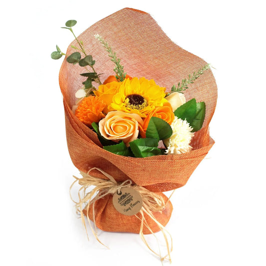 Ramo de flores de jabón en tonos naranja y amarillo, envuelto en tela de arpillera con un lazo de rafia y etiqueta.