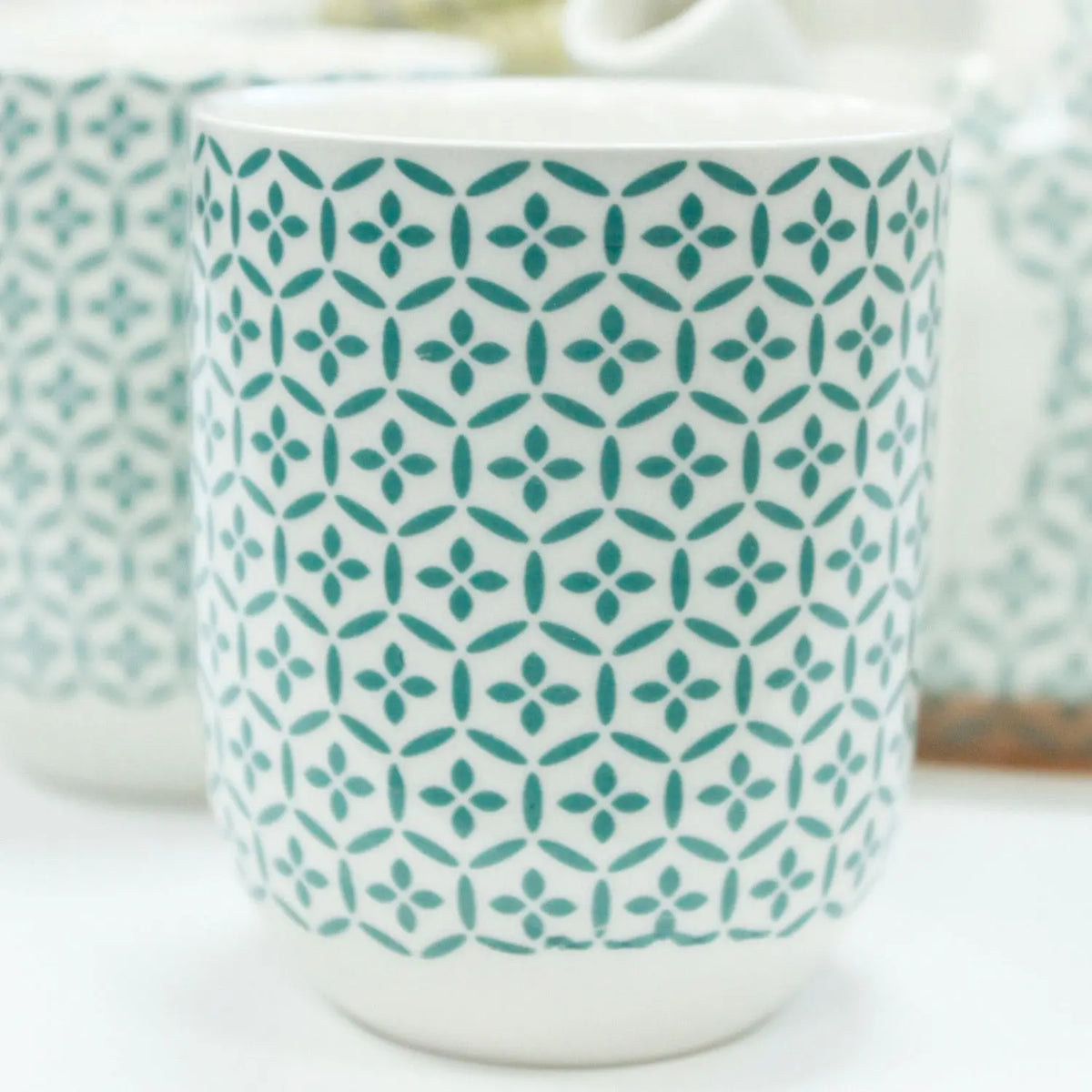 Juego de cerámica blanca con tazas y tetera decoradas con patrón geométrico de estilo mosaico en color verde azulado