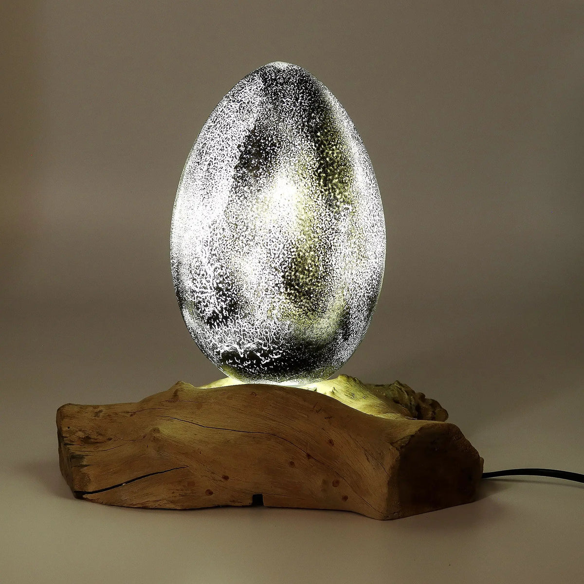 Lámpara con pantalla de cristal gris en forma de huevo con textura craquelada, sobre una base de madera natural.