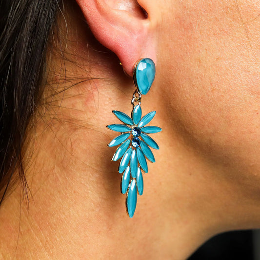 Pendientes largos colgantes con cristales turquesa en forma de gota y pétalos, con base metálica dorada.