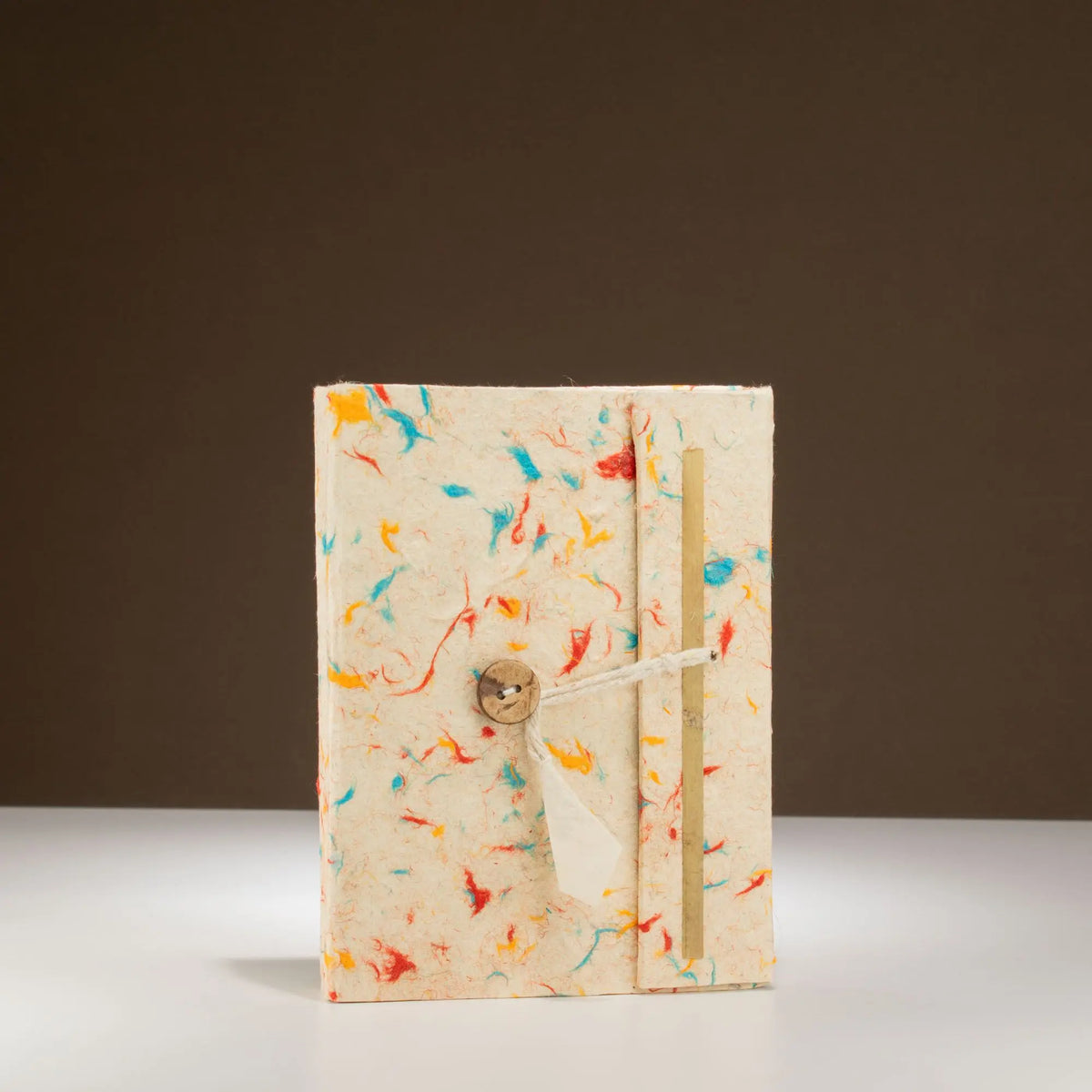 Cuaderno artesanal en tonos beige y colores vibrantes, con cierre de cuerda y detalle de madera.