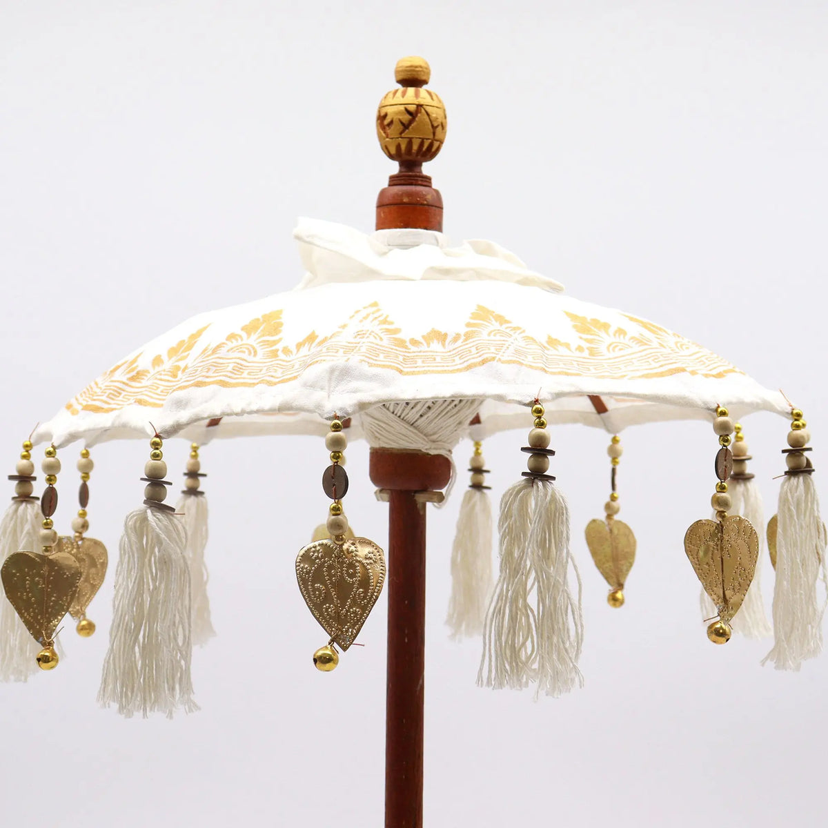 Sombrilla balinesa de lona blanca con detalles dorados, flecos, abalorios y remate tallado. Estilo artesanal elegante.