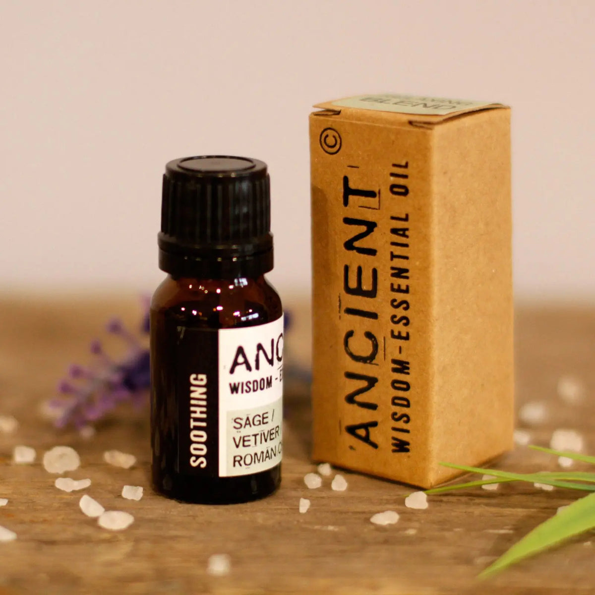 Frasco de aceite esencial oscuro de 10ml junto a su caja de cartón kraft sobre una mesa con cristales de sal y flores.