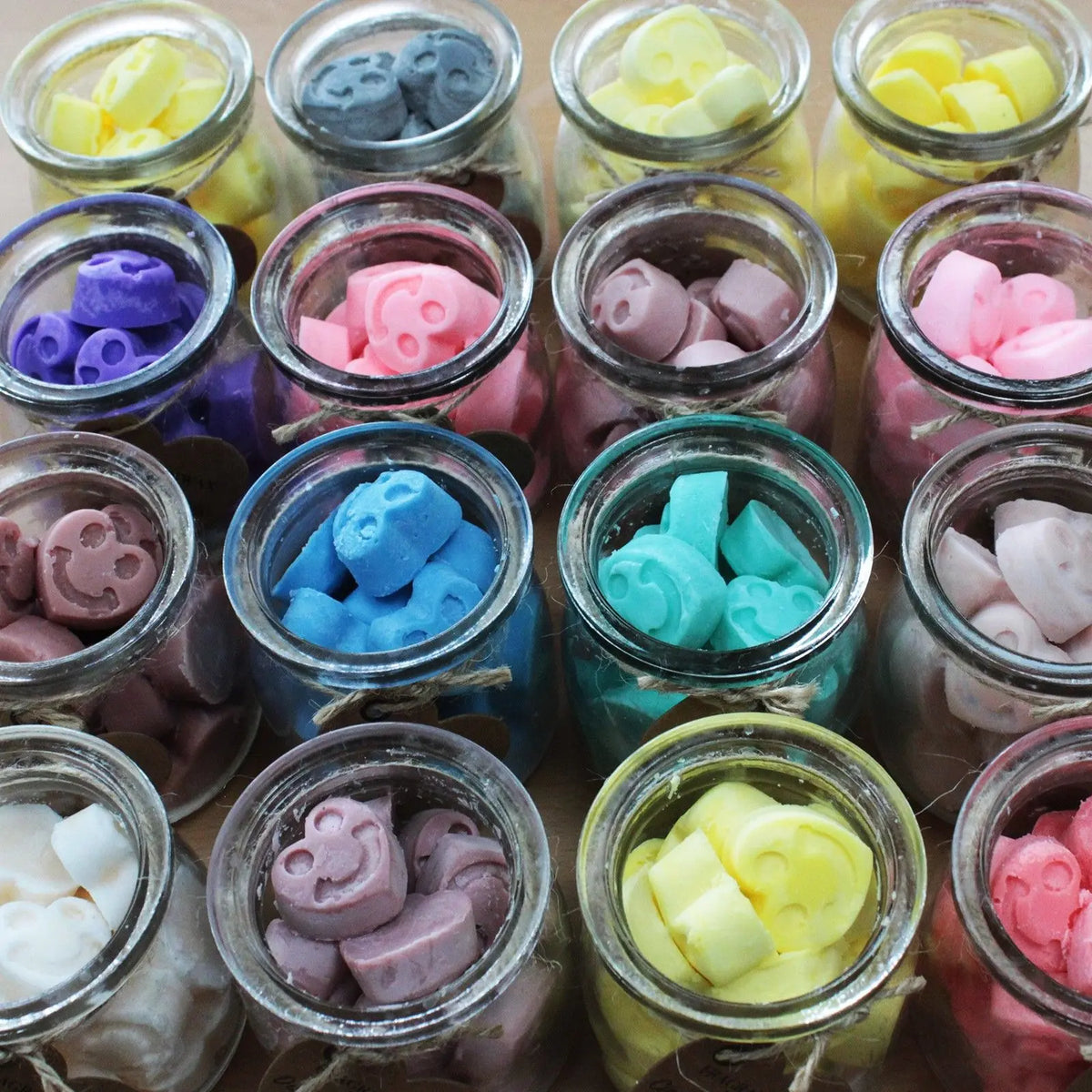 Frascos de vidrio con pequeñas figuras de cera de soja coloridas con forma de caras sonrientes. Vista superior.