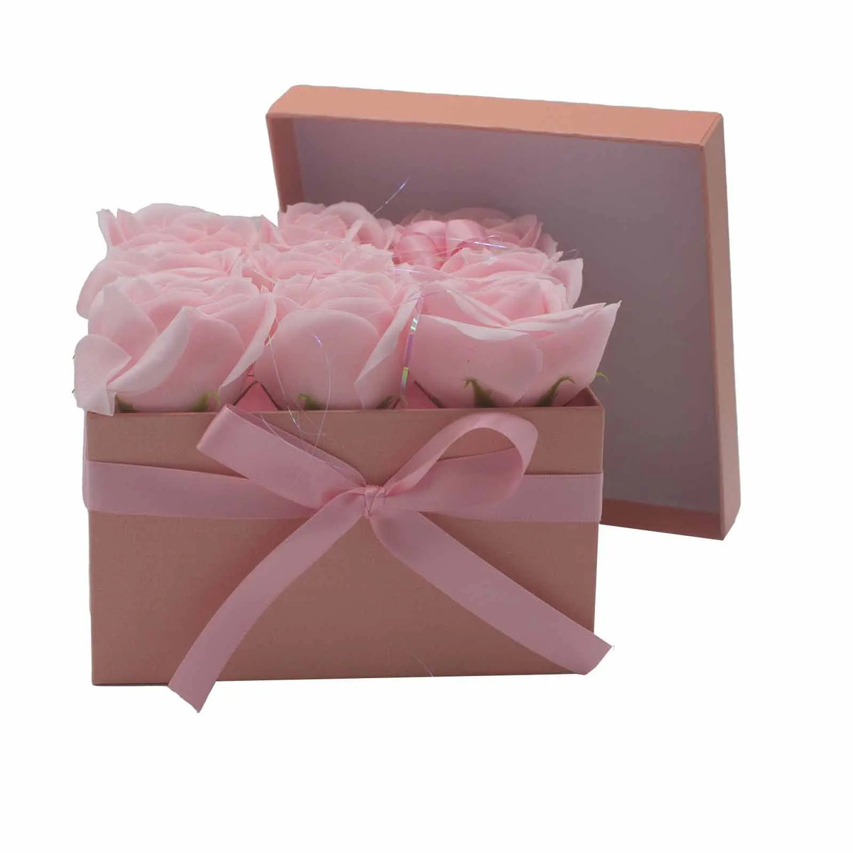 Caja cuadrada rosa con 9 rosas de jabón del mismo tono, decorada con un lazo de cinta rosa y su tapa apoyada detrás.