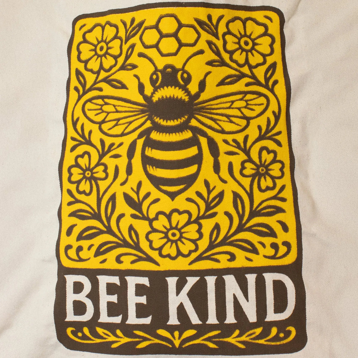 Diseño de bolsa de tela blanca con gráfico amarillo y marrón de abeja y flores, texto "BEE KIND".