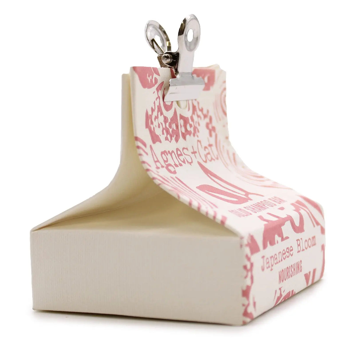 Champú sólido Agnes + Cat en caja de cartón color crema con estampado floral rosa, sujeta por una pinza metálica.