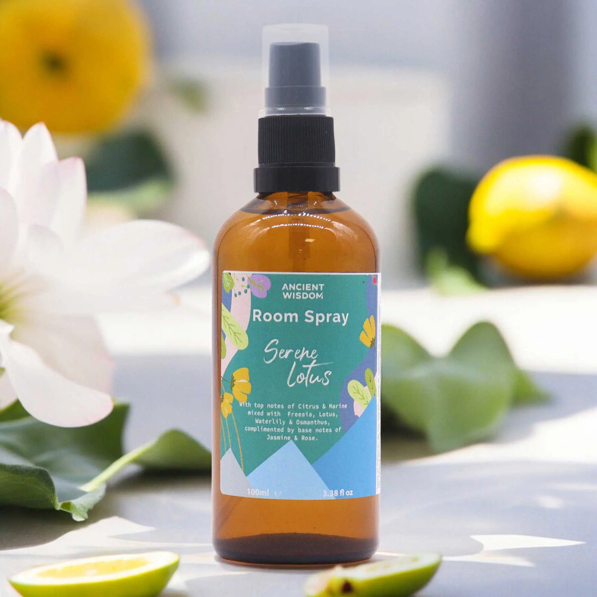 Frasco de vidrio ámbar con atomizador negro, etiqueta colorida con texto y flores de loto y limones de fondo.