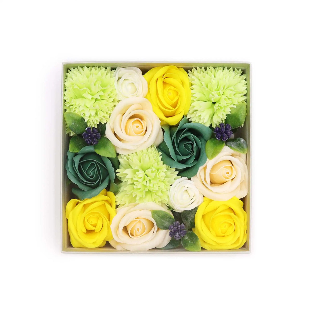 Caja cuadrada con flores de jabón en tonos amarillos, verdes y crema, decorada con hojas y pequeños frutos morados.