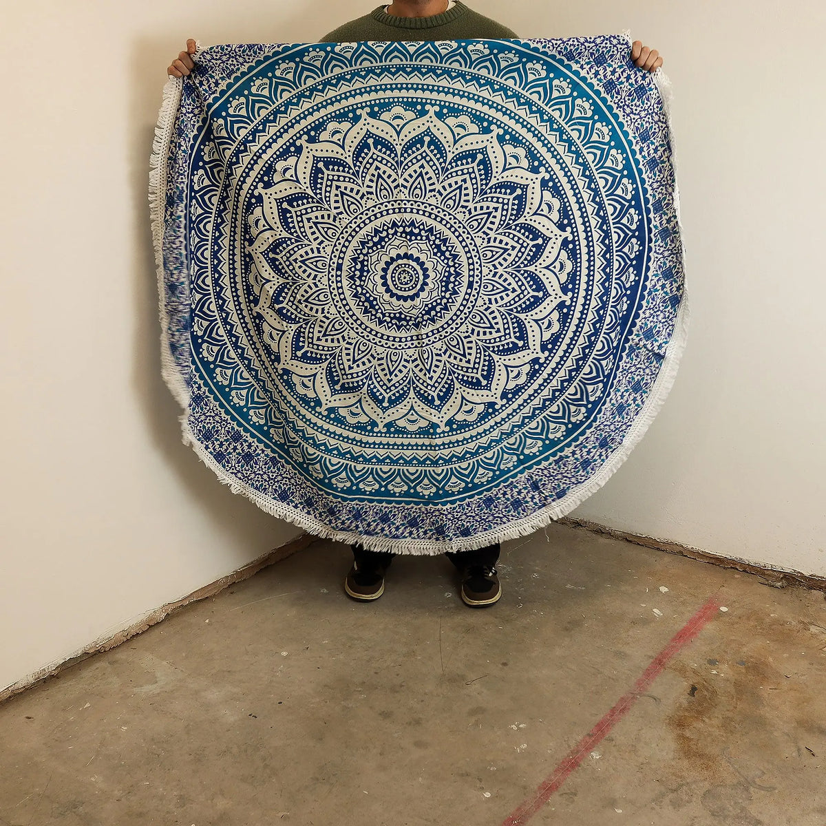 Tapiz redondo de algodón azul y blanco con estampado de mandala detallado y bordes con flecos sostenido por una persona.