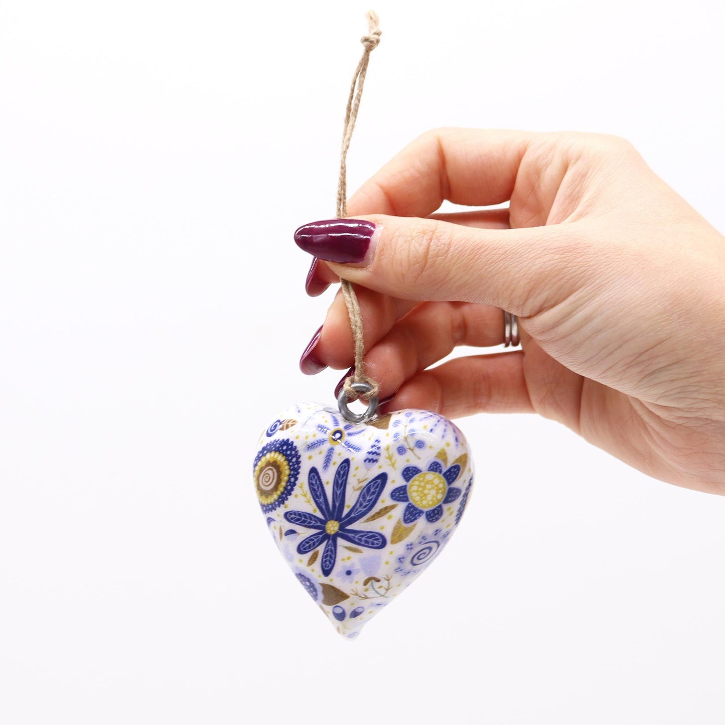 Corazón de cerámica blanca y azul con flores, colgado con cuerda, estilo artesanal.