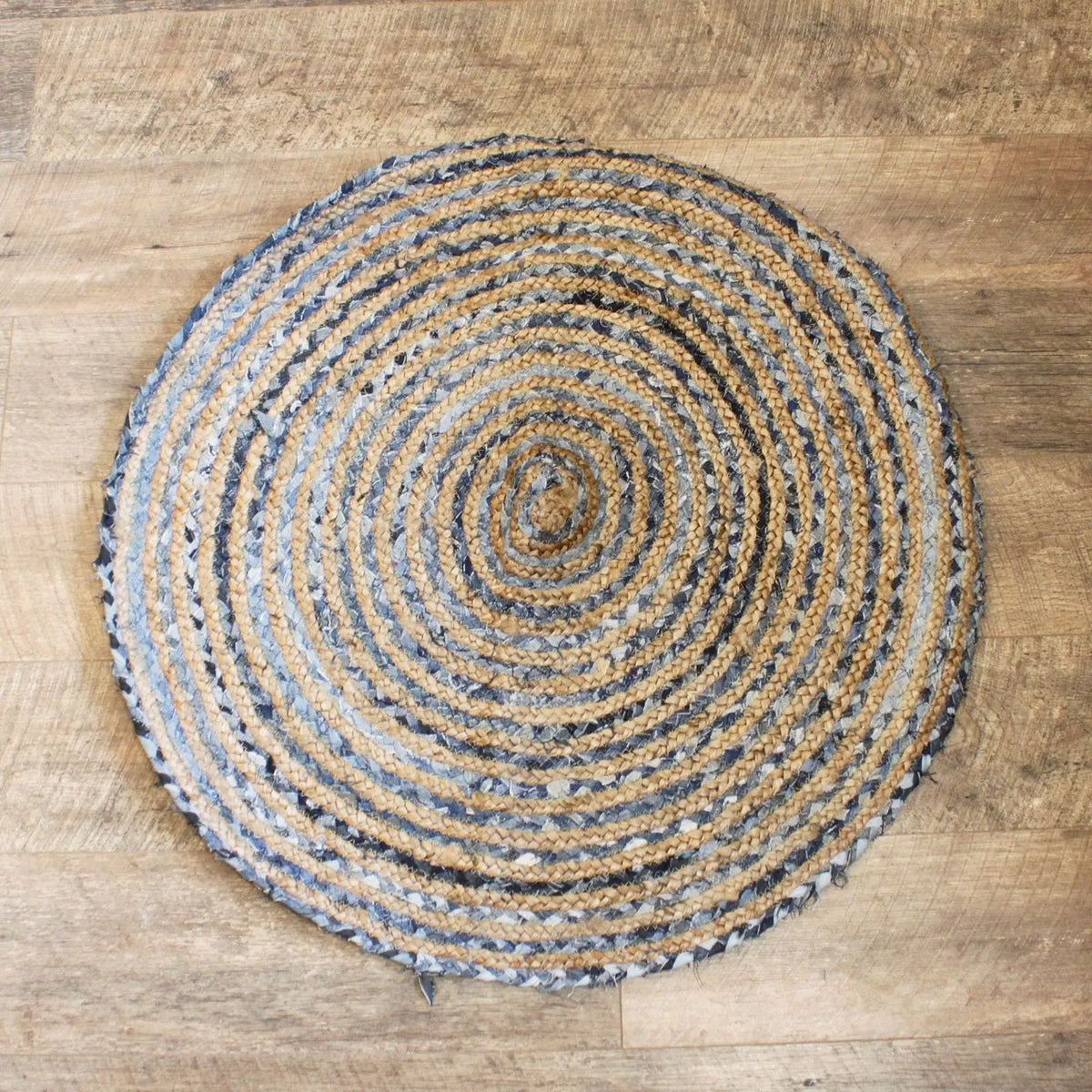 Alfombra redonda de 90 cm tejida en espiral con fibras de yute natural y mezclilla azul sobre suelo de madera.