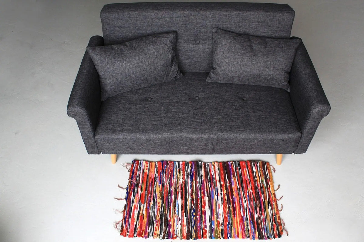 Alfombra de trapo artesanal estilo indio 50x90cm con franjas multicolores frente a un sofá gris moderno