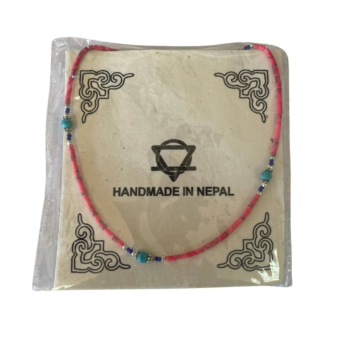 Collar artesanal de cuentas de coral rosa y turquesas sobre tarjeta decorativa con motivos tibetanos.
