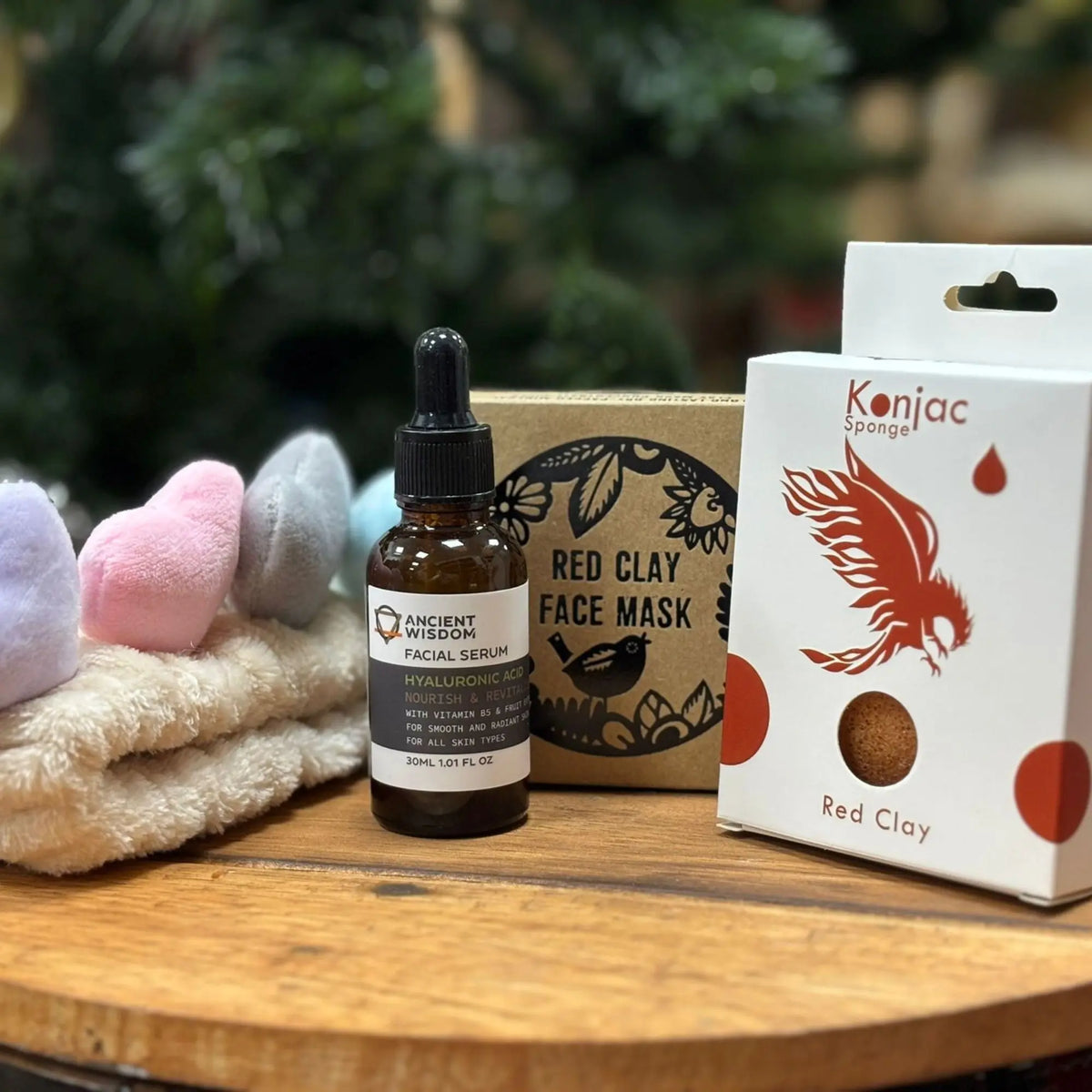 Set de belleza Ancient Wisdom: sérum facial, mascarilla de arcilla roja y esponja Konjac sobre mesa de madera.
