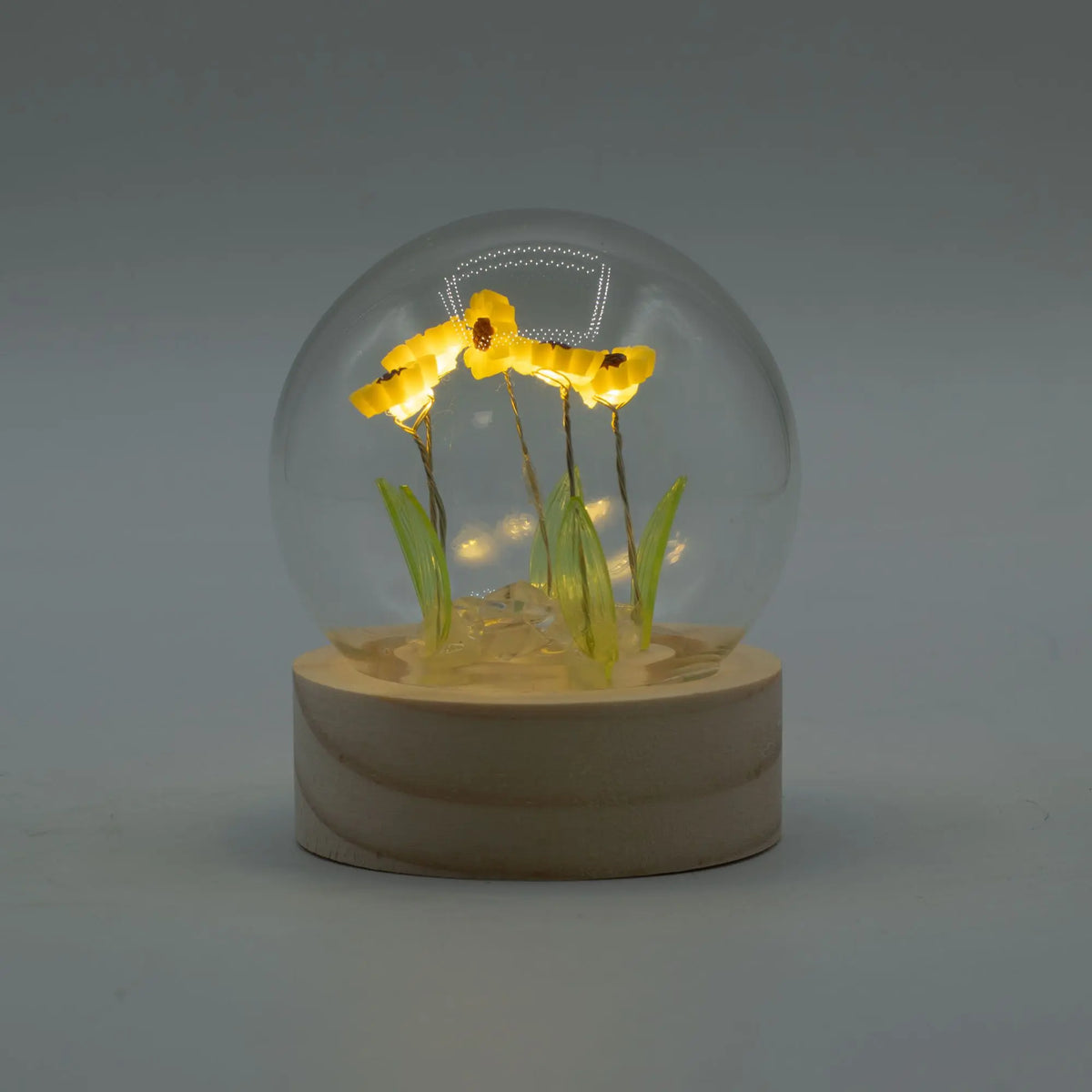 Domo de cristal sobre base de madera con cinco girasoles iluminados por luces LED cálidas en su interior.