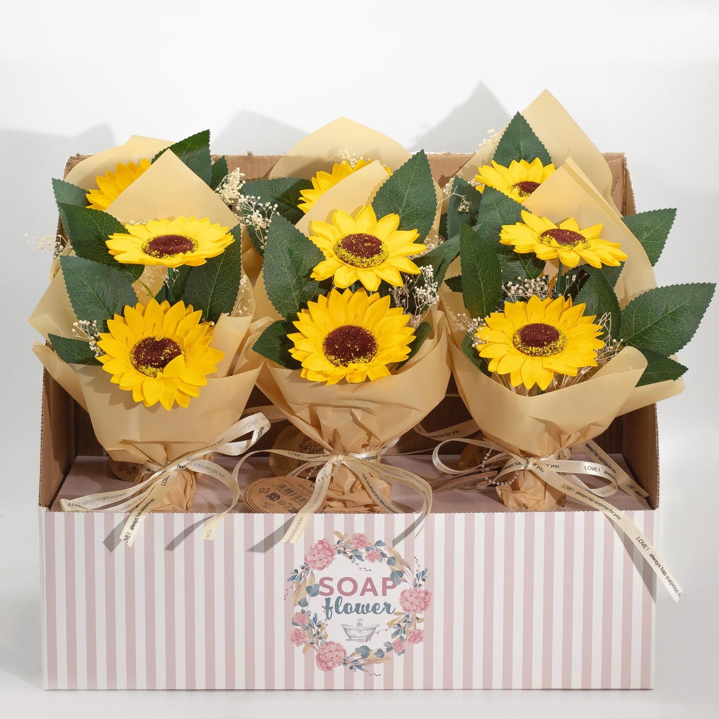 Ramos de dos girasoles de jabón en papel artesanal, con hojas verdes y detalles de flores blancas, dentro de una caja.