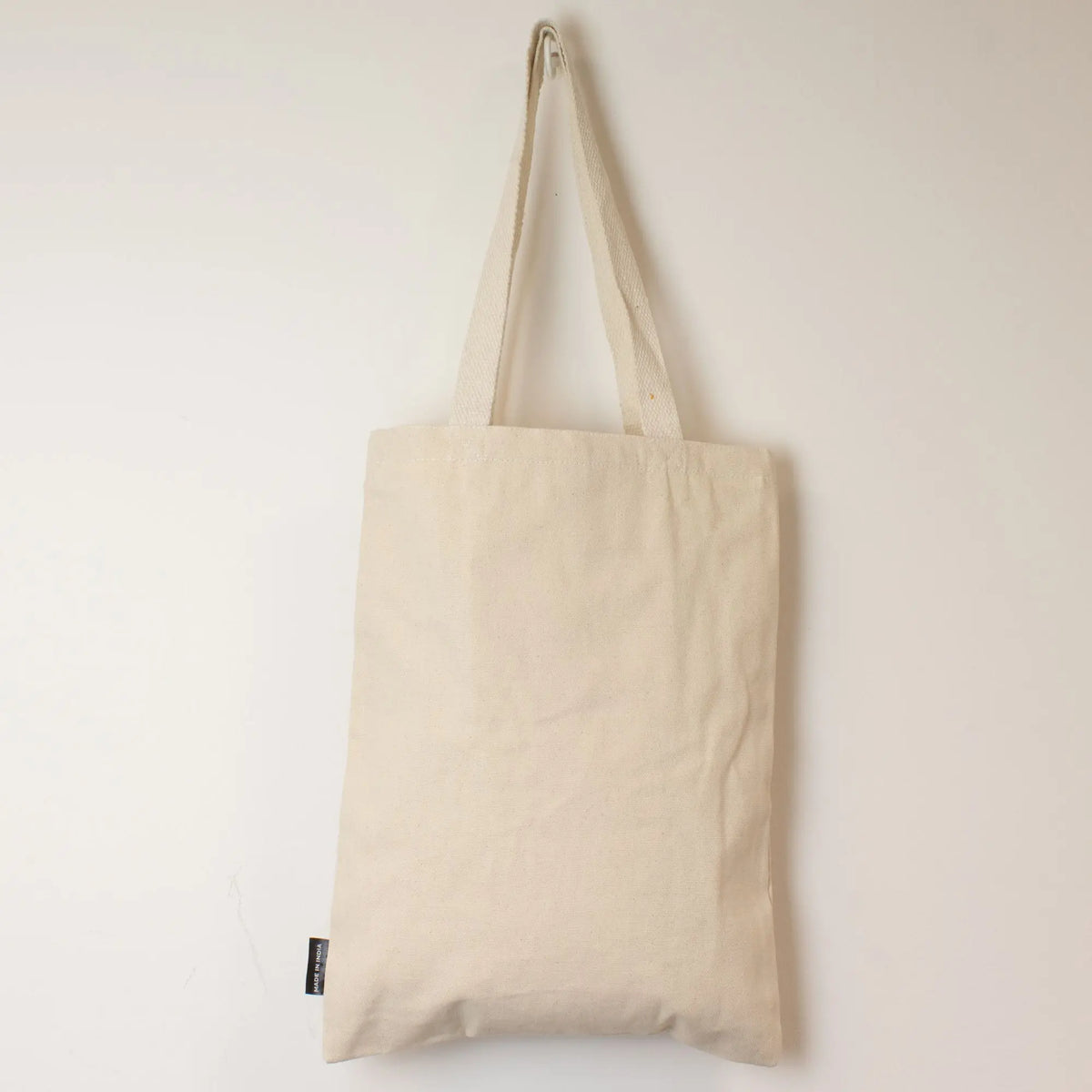 Bolsa de tela beige, estilo tote, fabricada en algodón, con asas largas y diseño minimalista.