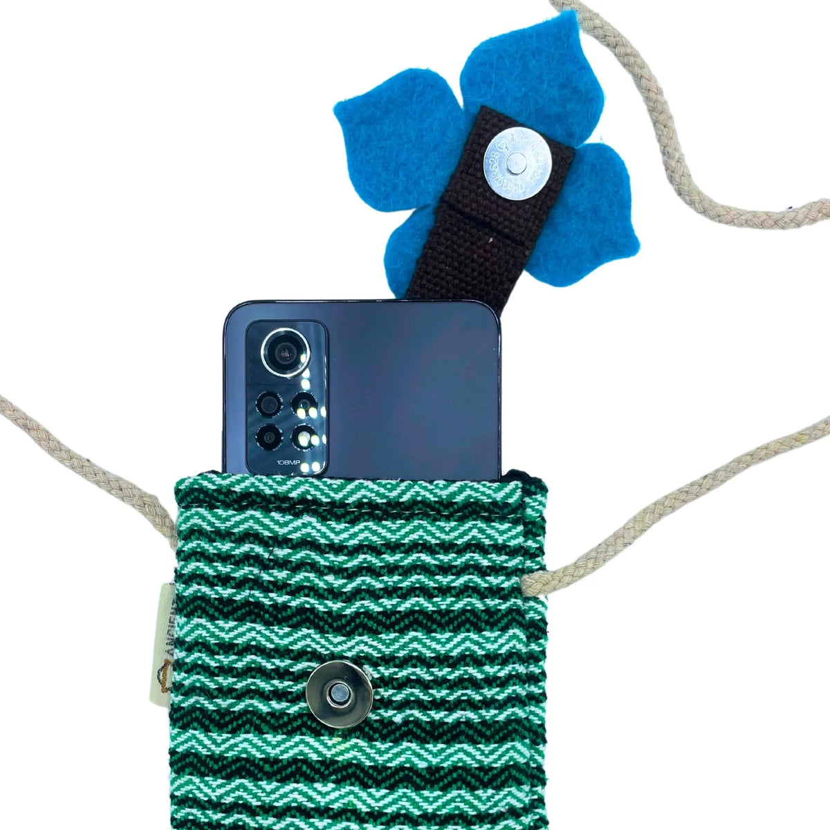Bolso de tela a rayas verdes y blancas con flor azul, correa de cuerda y teléfono negro en el interior.