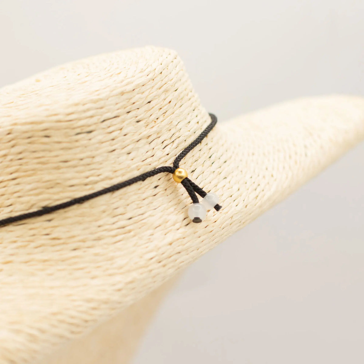 Sombrero de paja beige con cinta negra decorada con cuentas doradas y blancas, estilo bohemio y elegante.