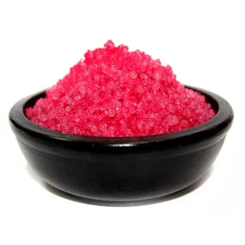 Cuenco negro de cerámica con gránulos aromáticos de color rosa intenso, dispuestos en forma de montaña sobre fondo blanco.