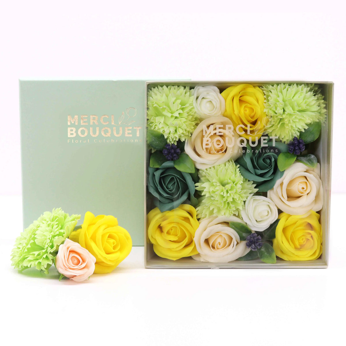 Caja cuadrada de regalo con flores de jabón en tonos amarillo, crema y verde, dispuestas con elegancia sobre fondo claro.