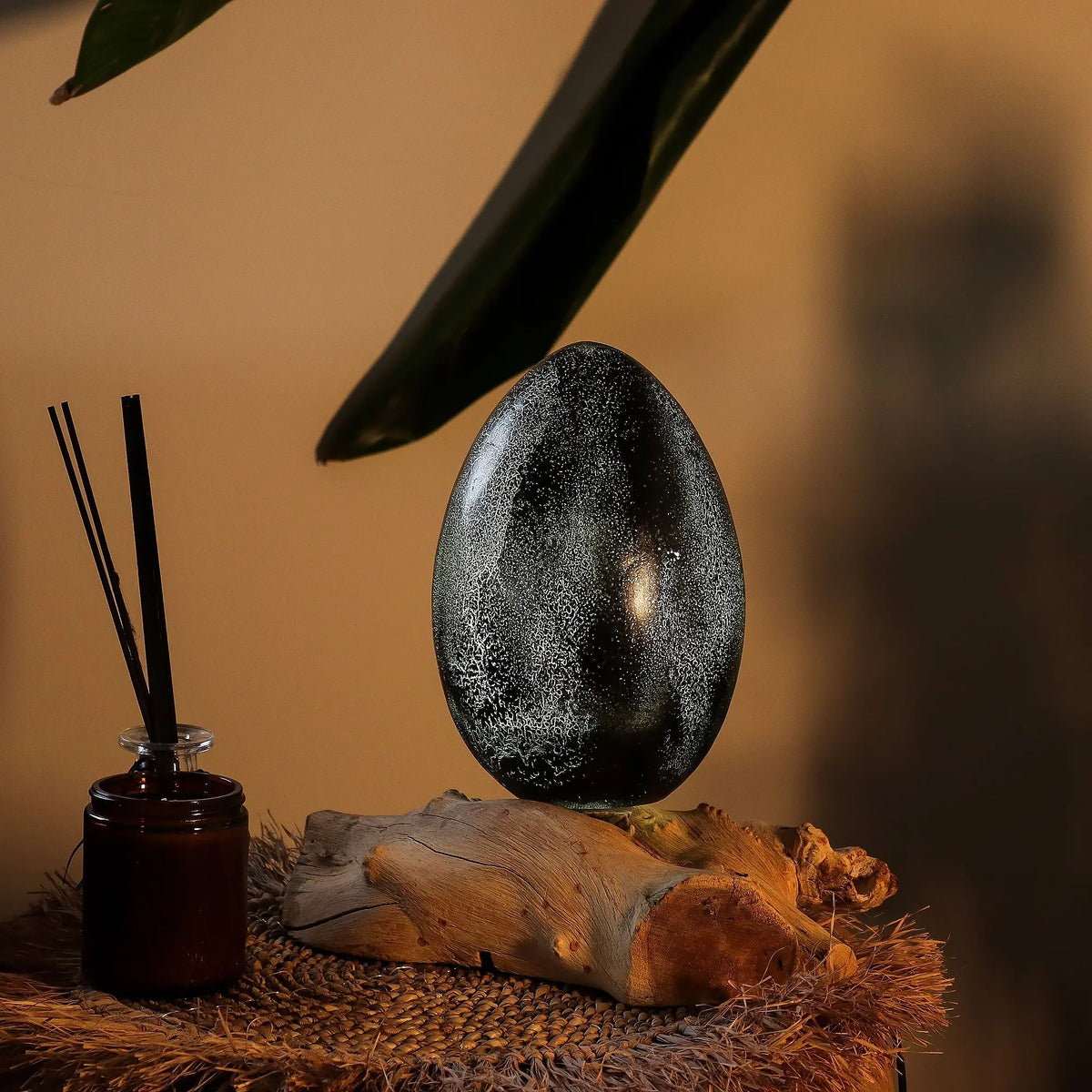 Lámpara de mesa gris con forma de huevo y textura craquelada sobre una base de madera natural.