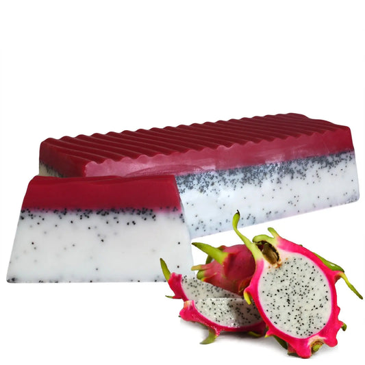 Jabón artesanal blanco y fucsia con semillas de amapola junto a frutas de dragón frescas sobre fondo blanco.
