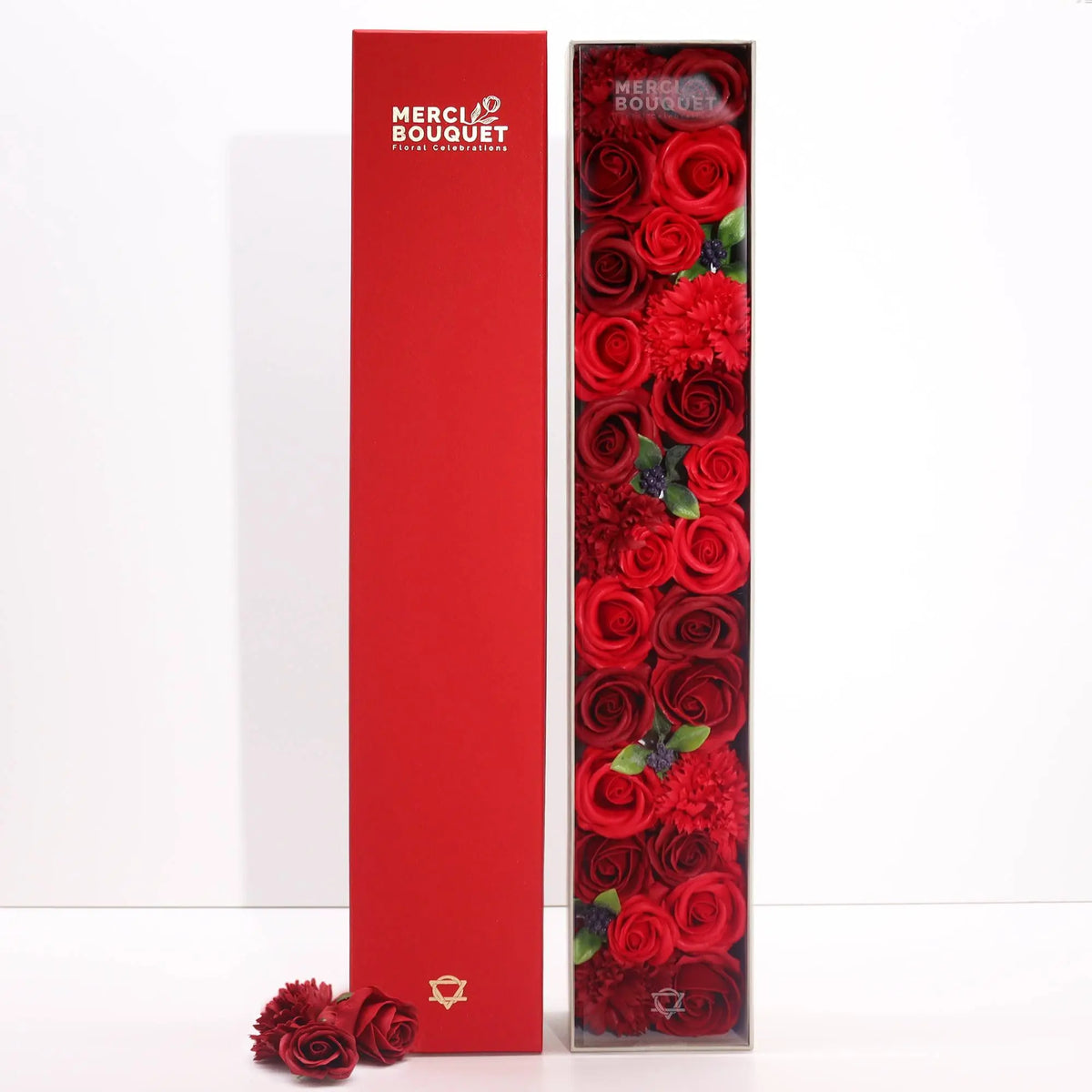 Caja rectangular con rosas rojas de jabón dispuestas verticalmente y una tapa roja a juego sobre fondo blanco