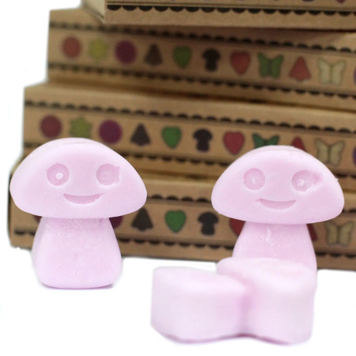 Ceras de soja rosas en forma de champiñón sonriente frente a cajas de regalo de cartón decoradas.