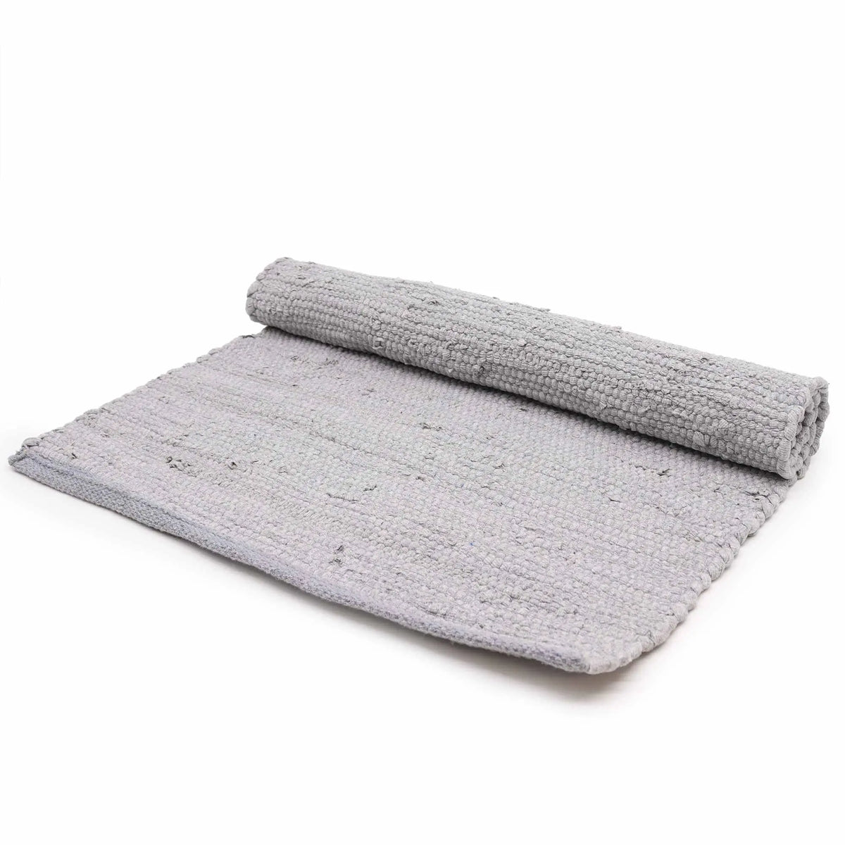 Alfombra de algodón gris tejida a mano, rectangular y parcialmente enrollada, con textura granulada sobre fondo blanco.