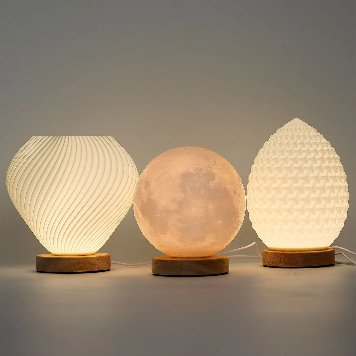 Tres lámparas LED de diseño escultural sobre bases de madera, con texturas geométricas y efecto de luz de luna.