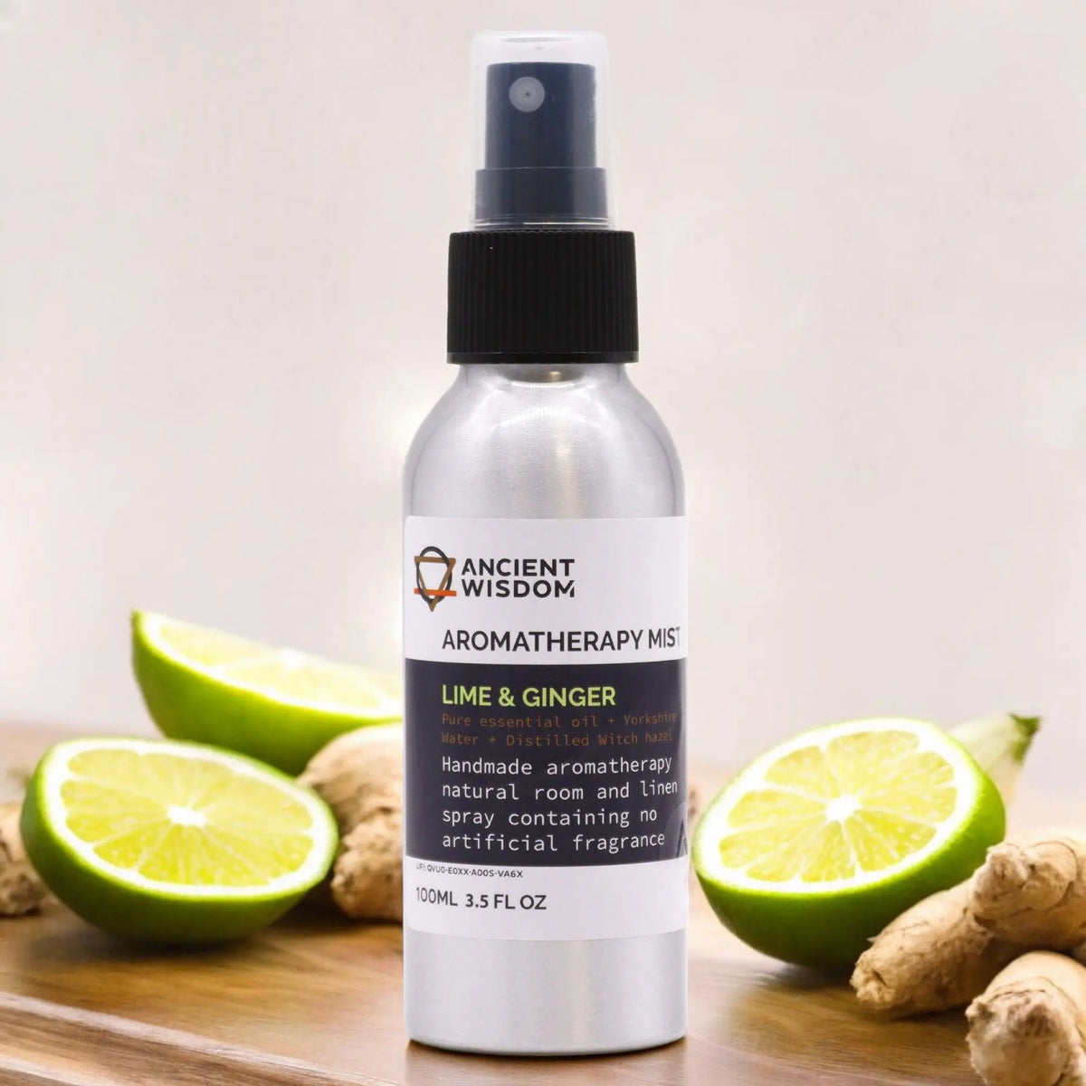 Botella de spray plateada de 100ml con etiqueta de lima y jengibre sobre tabla de madera con rodajas de lima y jengibre.
