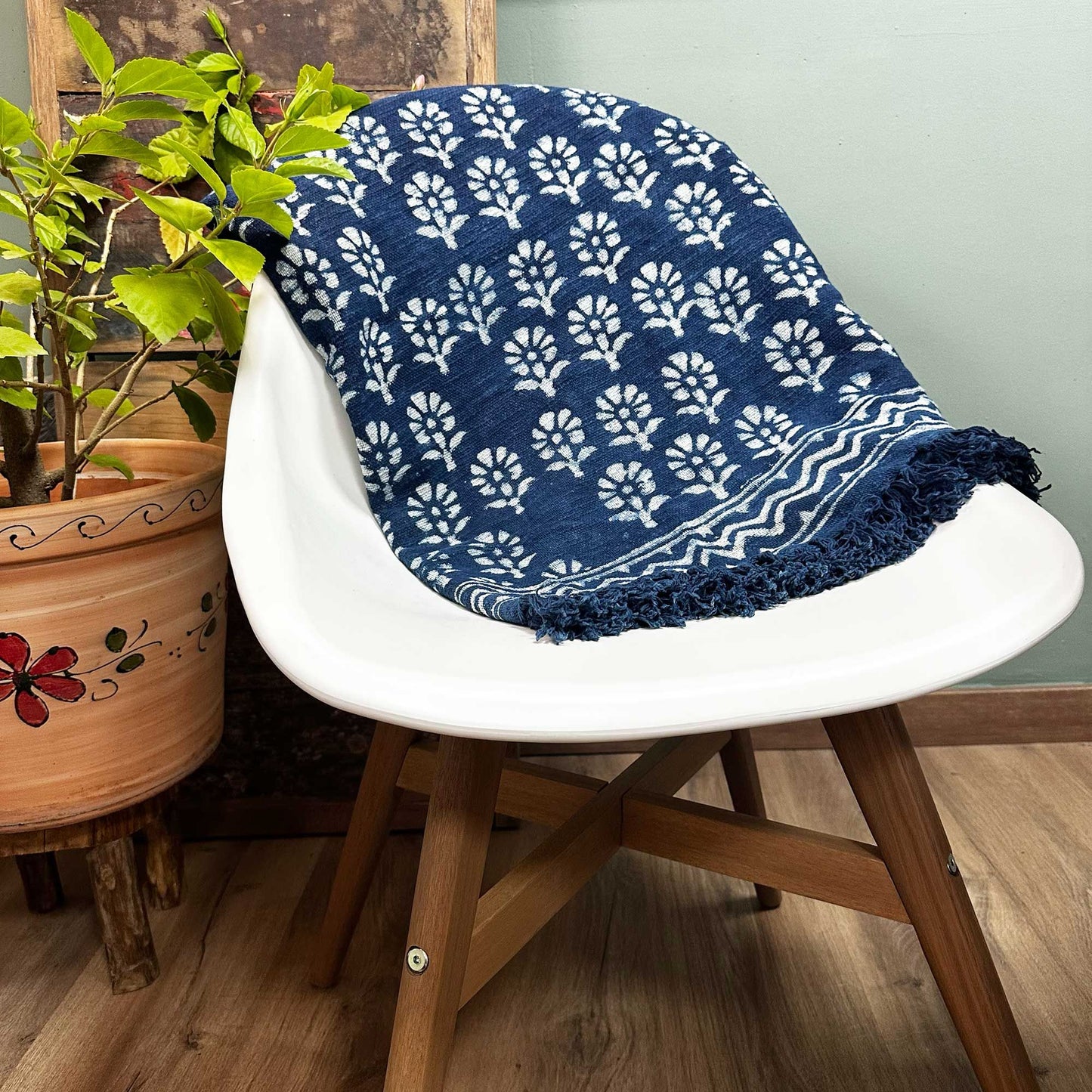 Manta azul marino con estampado blanco, algodón, estilo bohemio, con flecos, sobre silla moderna y planta decorativa.