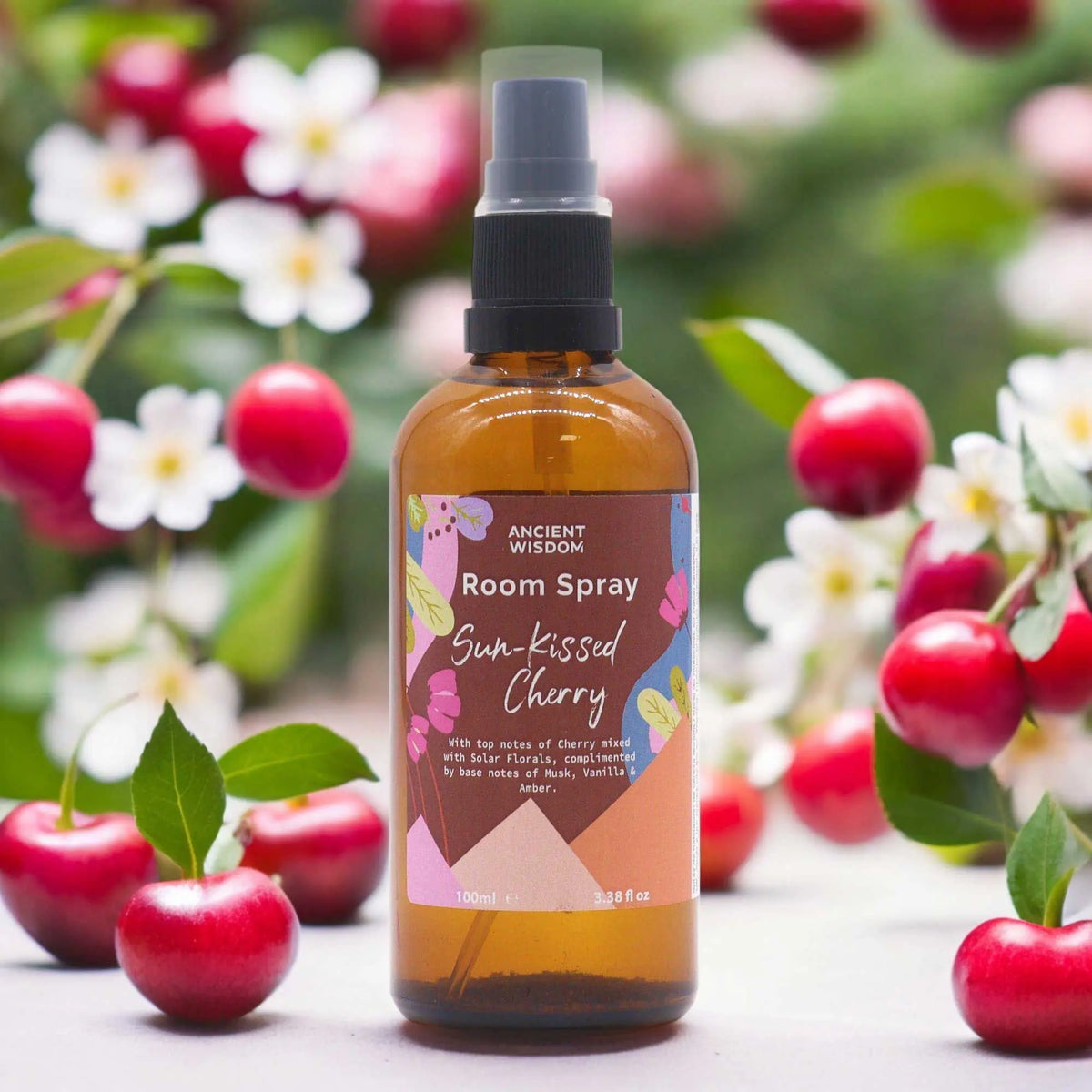 Spray de ambiente de 100ml en botella de vidrio ámbar, rodeado de flores blancas y cerezas rojas frescas.