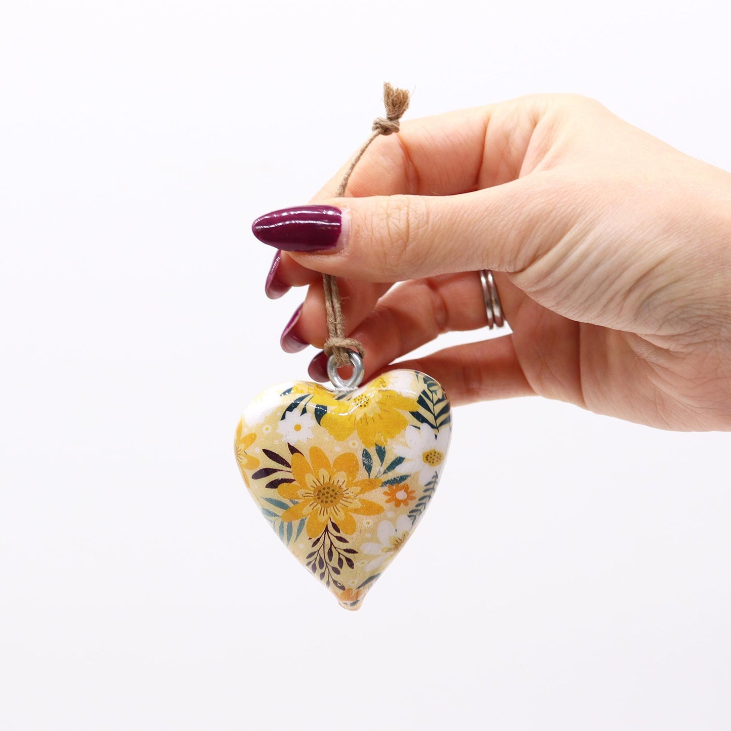 Corazón decorativo de cerámica blanca con flores amarillas y verdes, colgado con un cordón de yute.