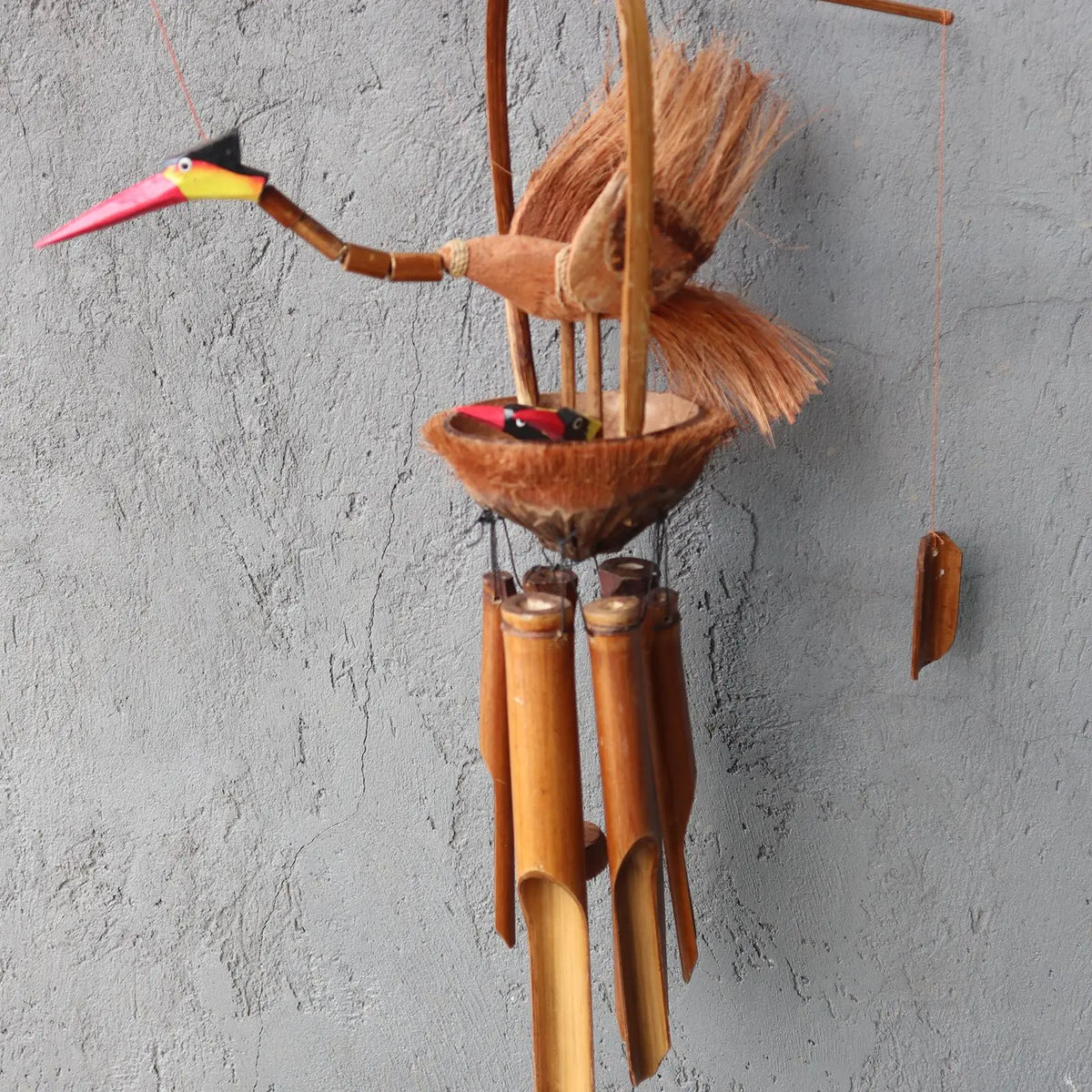 Campana de viento de bambú y coco con diseño artesanal de madre pájaro y crías en colores naturales sobre fondo gris