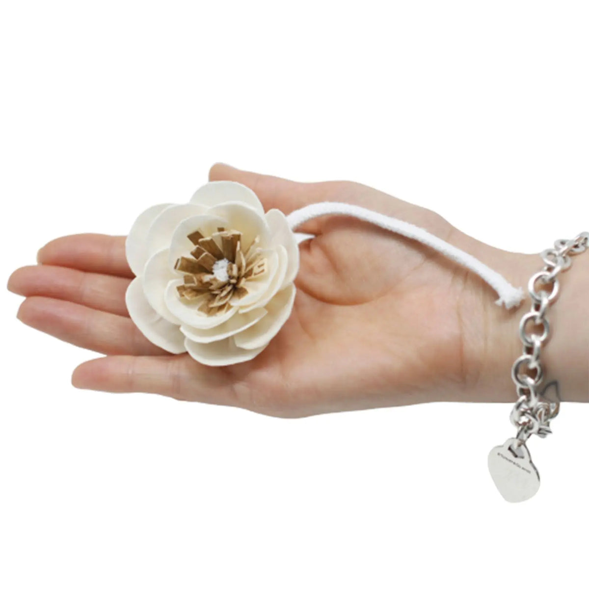 Flor difusora de madera color crema con centro marrón, unida a una cuerda blanca, sostenida sobre una mano humana.