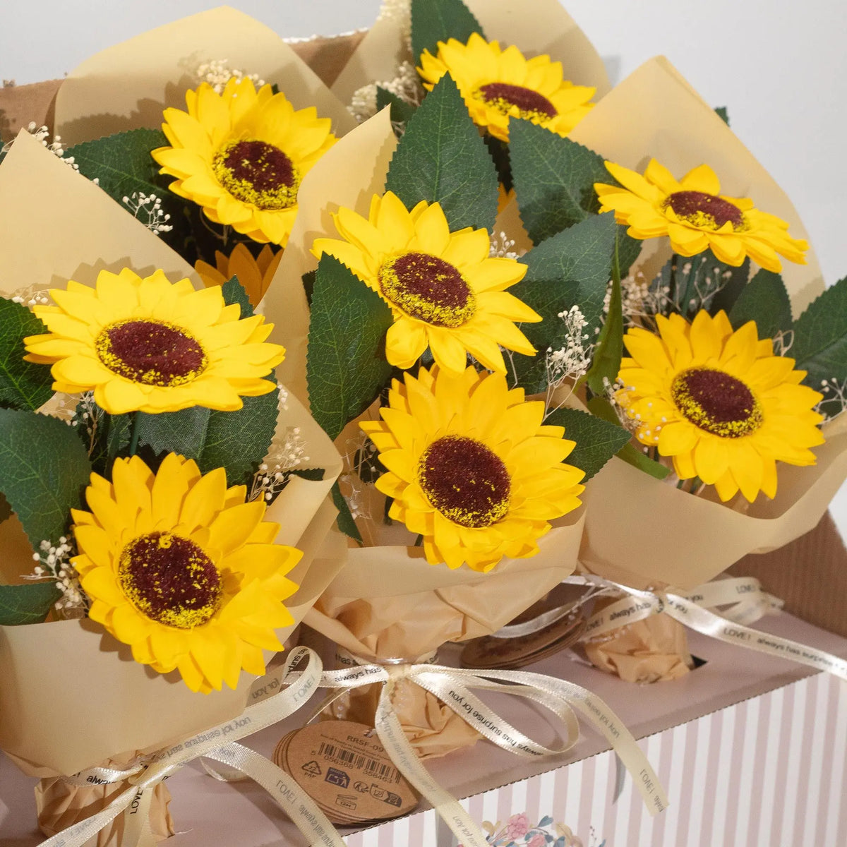 Ramos de dos girasoles de jabón amarillo con hojas verdes, envueltos en papel craft y lazo, listos para regalo.