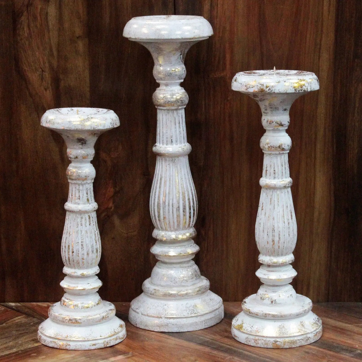 Tres candelabros vintage de madera en blanco y oro con acabado envejecido sobre superficie de madera oscura