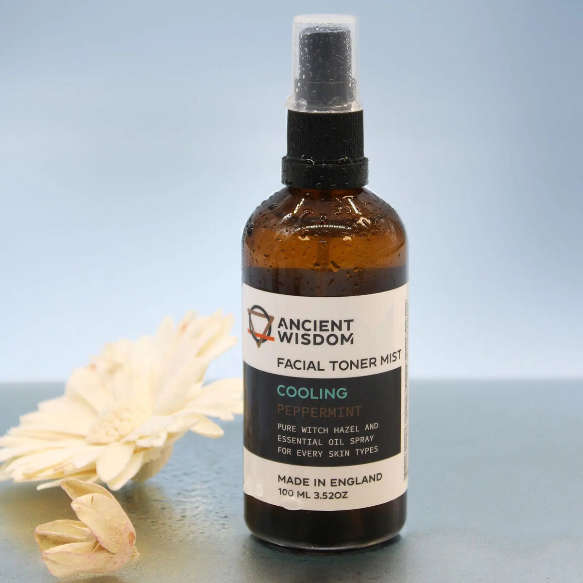 Frasco de vidrio ámbar de 100ml con atomizador negro, etiqueta de tónico facial de menta y flores blancas de fondo.