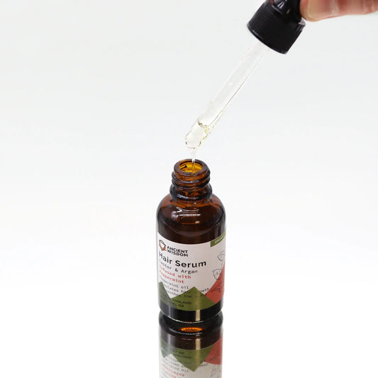 Frasco de vidrio ámbar con gotero aplicando serum capilar sobre fondo blanco minimalista