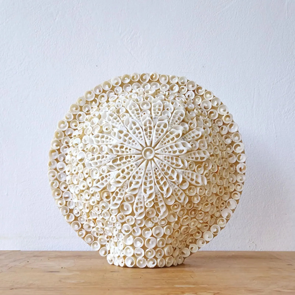 Lámpara redonda estilo boho hecha a mano con pequeñas conchas blancas dispuestas en un patrón floral detallado.