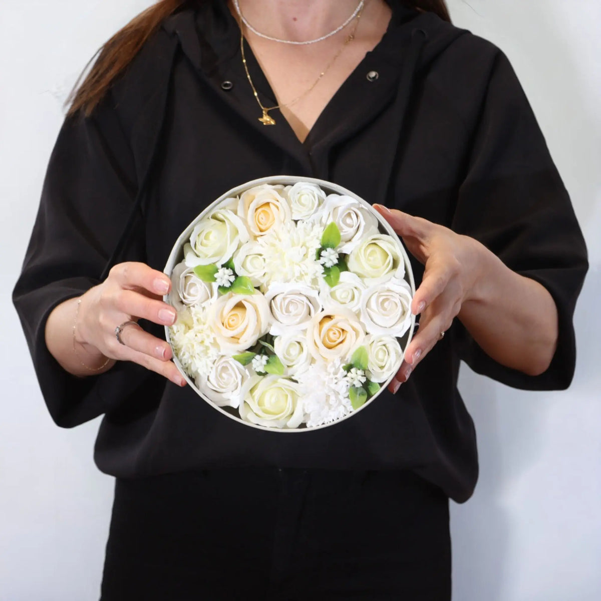 Persona sosteniendo una caja redonda con flores de jabón blancas y marfil, estilo elegante para regalo de bodas.